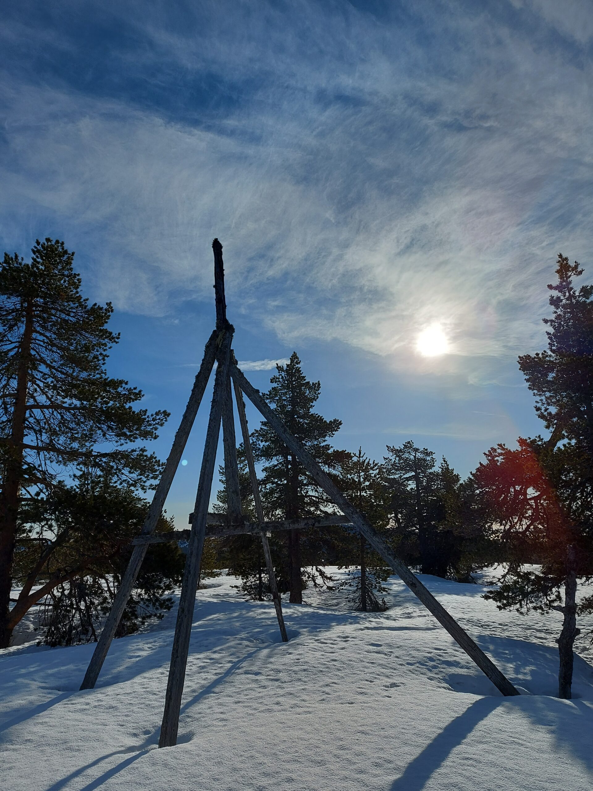 trigonometrisk punkt i tre på snø med sol og blå himmel